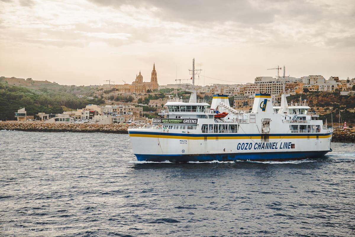 a Gozo Channel ferry leaving the harbour with a village in the background